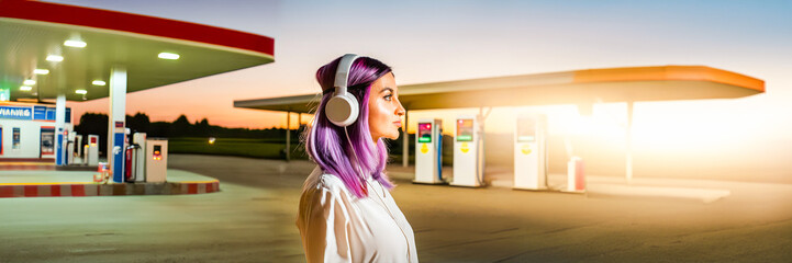 woman wearing headphones in a retro gas station with sunset