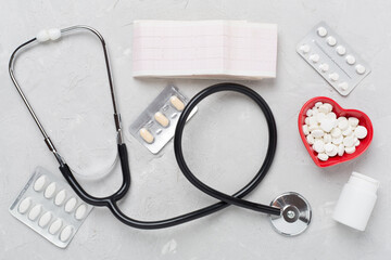 Stethoscope with heart medicines on concrete background, top view