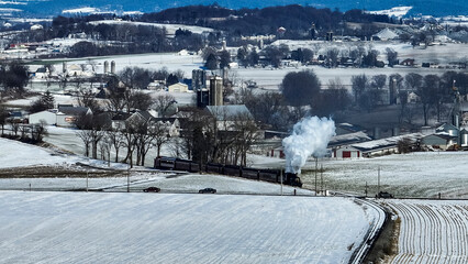 A train is traveling through a snowy countryside. The train is black and white and is the only thing visible in the image