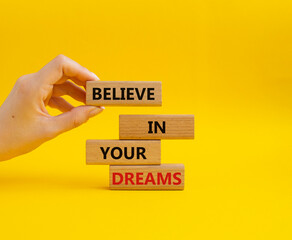 Believe in your Dreams symbol. Concept words Believe in your Dreams on wooden blocks. Businessman hand. Beautiful yellow background. Business and Believe in your Dreams concept. Copy space