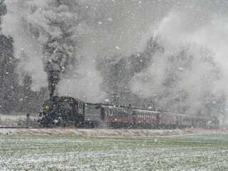 A train is traveling through a snowy field. The steam from the train is visible in the air,...