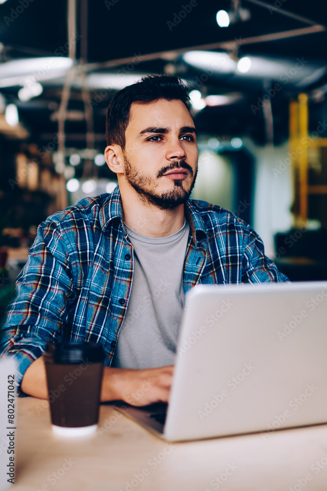 Poster thoughtful male freelancer pondering on idea for working project sitting with laptop computer in cow