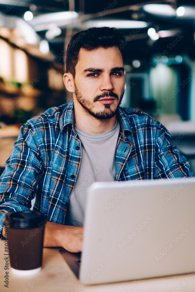 Poster portrait of serious hipster guy making research for exam preparation using netbook and wifi in colle