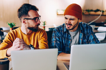 Annoyed hipster guy communicating with colleague about  problem with cooperation sitting with...