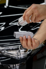 Specialistic ceramic coating liquid poured onto sponge by unrecognizable professional in protective gloves. Car detailing process. Black car in the background.