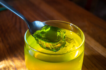 Green jelly in a glass cup. An iron spoon stuck in jelly