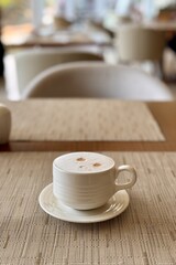 A coffee cup is placed on a saucer, resting on a wooden table. The tableware includes dishware and drinkware, making it a perfect setting for enjoying a hot drink