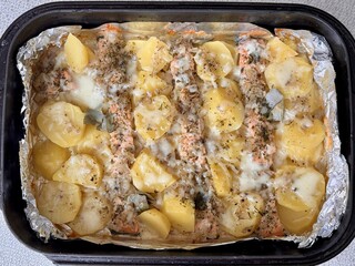 Baked salmon fish steaks with potatoes under mayonnaise lie on baking paper on a black baking sheet. Delicious fast food baked in the oven