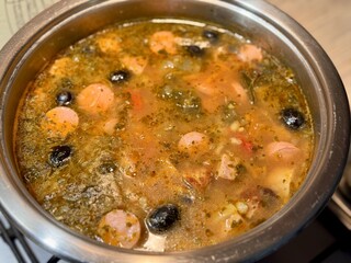 Delicious soup hodgepodge in a stainless pan is cooked on a gas stove at home. Close-up