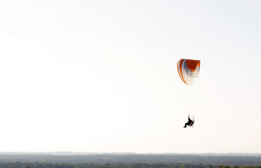 Silhouette of a man flying a motorized paraglider over a flat landscape. Extreme outdoor sports...