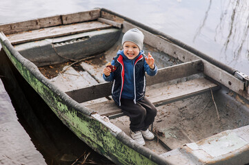 Little boy, happy smiling child sitting on an old abandoned boat with cookies in his hands. Photography, nature.