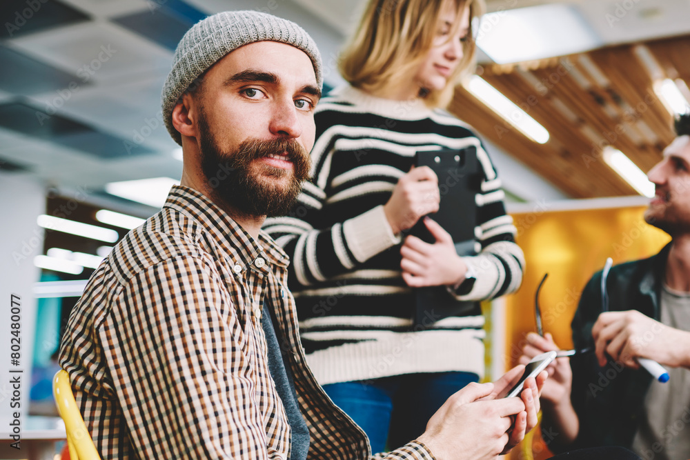 Poster half length portrait of handsome bearded employee in cool hat downloading application from network o