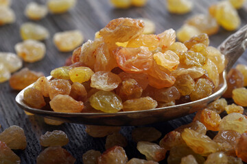 golden raisins in a spoon on a wooden table. dried grapes. close up