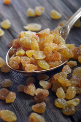 golden raisins in a spoon on a wooden table. dried grapes. close up