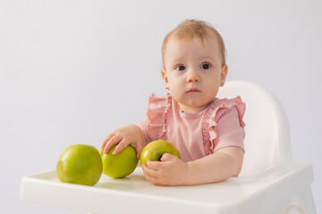 Cute baby in a baby chair nibbles apples on a white background