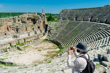 A male tourist enjoys a walk through the amphitheater among the ruins of the ancient city of Perge,...