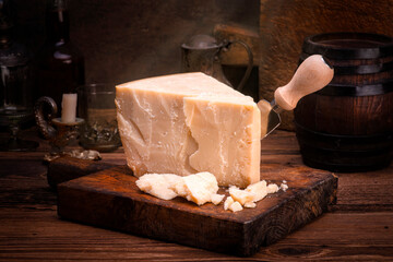 Traditional Parmesan cheese piece with cheese knife during food preparation as a close-up on a rustic wooden cutting board