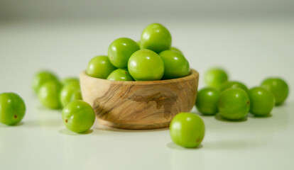 Green plums. A bowl of fresh unripe plums on a white background. Fresh raw green plum in wooden...