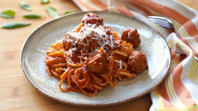 Woman sprinkling parmigiano reggiano  cheese on Homemade Italian spaghetti and meatballs in tomato sauce on wooden table