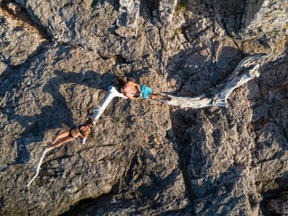 TOP DOWN: Happy couple enjoys sunlit rocky shores, lying on a piece of driftwood
