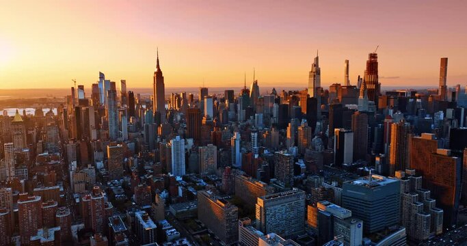 Pink light of setting sun covering the facades of diverse buildings in the downtown of New York. Stunning view of metropolis at golden hour from top.