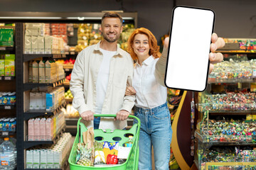 Excited couple showing big smartphone with empty screen at store, mockup for design, spouses...