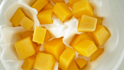 Fresh mango pieces falling into yoghurt cream, top down view