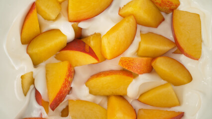 Fresh nectarines pieces falling into yoghurt cream, top down view