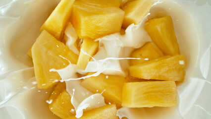 Fresh pineapple pieces falling into yoghurt cream, top down view