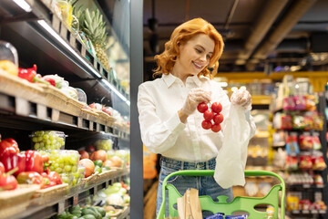 European woman choosing fresh organic tomatoes, buying vegetables and products in supermarket. Consumerism concept