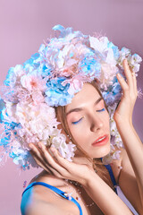 A beautiful woman with a wreath of flowers in a blue swimsuit on a pink background