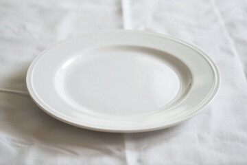 A plain white plate on a plain white tablecloth.