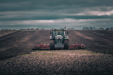 Tractor with cultivator working on a field under dark moody sky