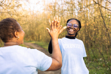 African american women sharing high five and being happy with the results of the team, congratulating each other after finishing forest litter cleanup. Proud and satisfied with their work.