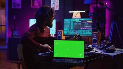 Guitarist playing his acoustic instrument next to greenscreen on laptop, learning new strings accords to play on guitar in home studio. Musician artist developing his singing skills. Camera B.