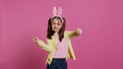 Obraz premium Confident cheery girl showing dance moves in the studio, feeling cheerful and positive about easter holiday festivity. Talented child dancing around and wearing bunny ears. Camera B.