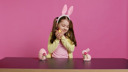 Joyful little girl playing with festive easter decorations in studio, creating arrangements with a...