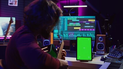 Sound engineer practices playing acoustic guitar using learning app tutorial on phone via greenscreen isolated display. Young musician learning to play instrument with online lessons. Camera B.