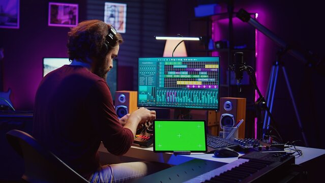 Musician mixing and mastering sounds at home studio with electronic console and soundboard, creating modern tunes. Sound engineer producing audio tracks with greenscreen on tablet. Camera B. - Powered by Adobe