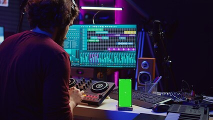 Sound engineer working on mixing and mastering techniques in his home studio, using phone with...