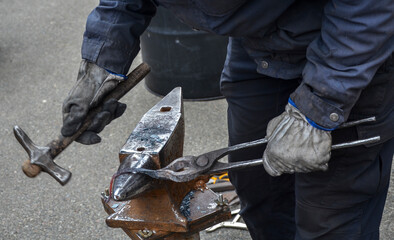 Close-up view of a skilled blacksmith with hammer and tongs ready to strike a piece of hot metal...