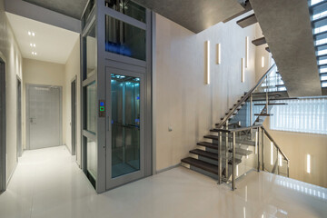A spacious, bright hall of a private house with a staircase and a glass elevator.