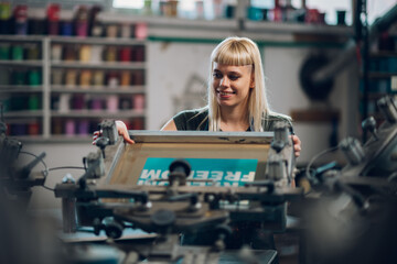 Female graphic worker putting screen printing plate on printing press.