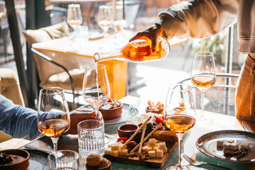 Pouring rose or amber wine at a dinner party with friends in a bar or restaurant.