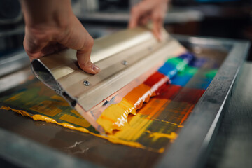 Close up of print shop worker's hands using squeegee for screen printing