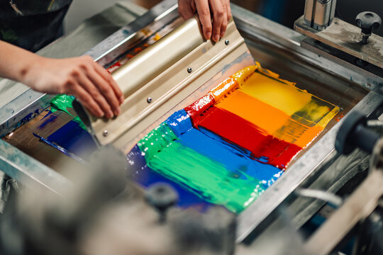 Graphic technician's hands silkscreen printing with squeegee.