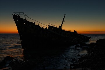 This image portrays the haunting silhouette of a shipwreck against a dramatic sunset backdrop, conjuring a sense of adventure and demise