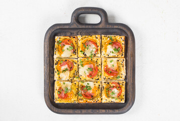 Mini square snack pies with tomatoes, ham, mozzarella, pesto, sesame seeds. On a wooden plate. Top view