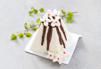 Easter Holiday. Ricotta cream dessert with chocolate. Decorated with white marshmallow flowers. With birch twigs. On a plate. Close-up
