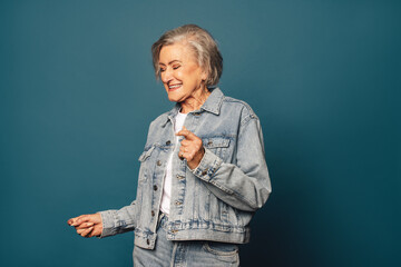 Mature woman dancing in casual denim on blue backdrop.